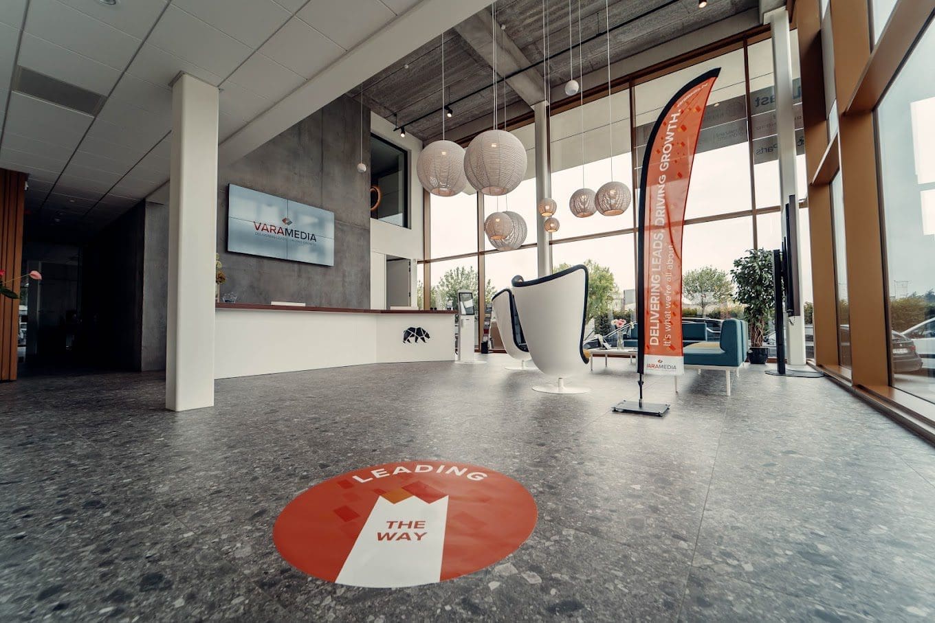 varamedia-inkom Moderne kantoorlobby met 'Leading the Way' vloersticker en oranje beachvlag