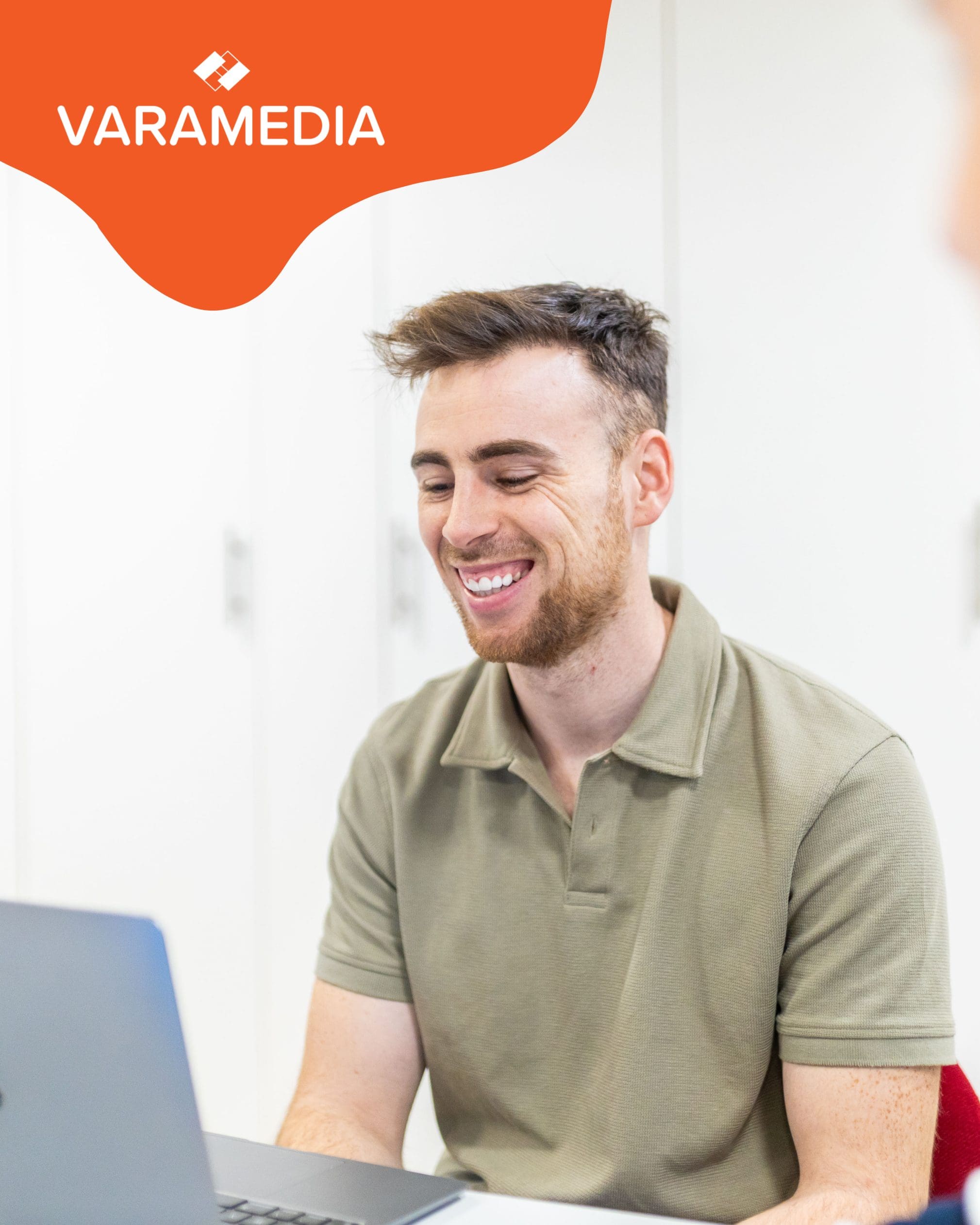 Lachende man achter laptop met Varamedia-logo op de achtergrond