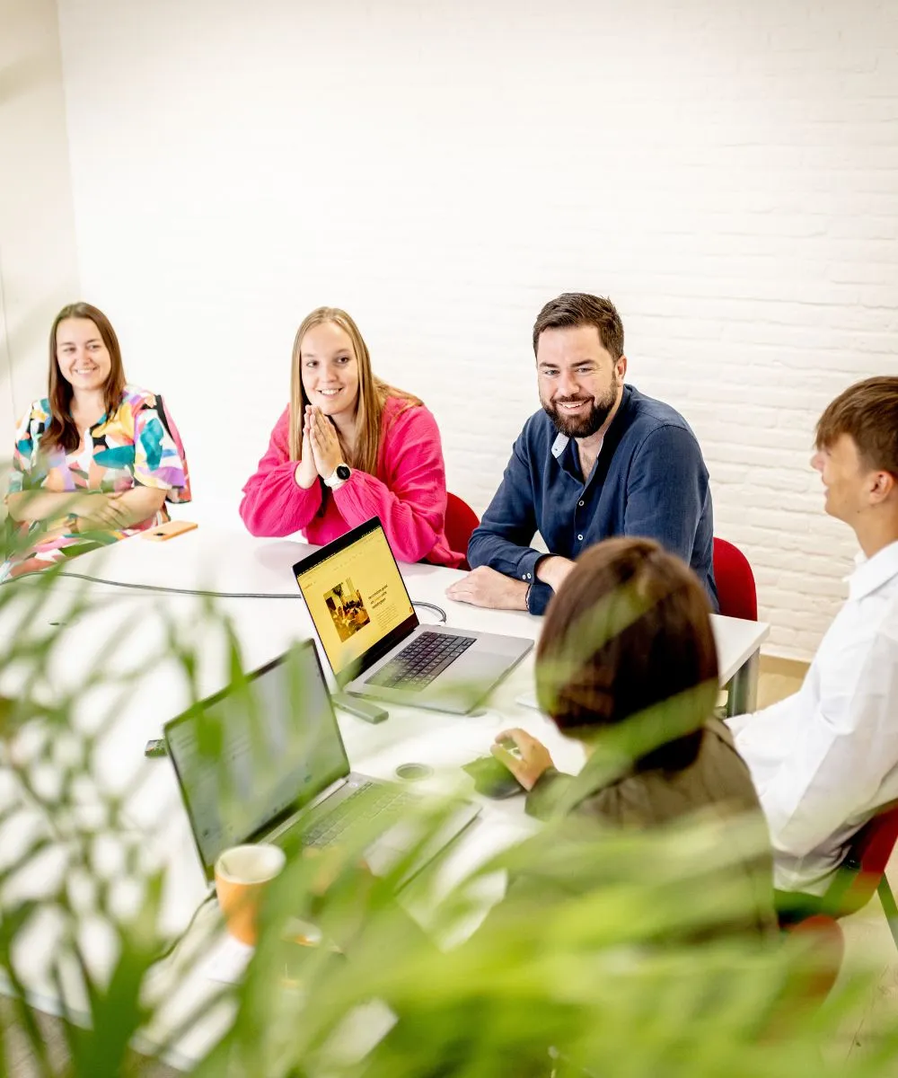 Lachend team rond vergadertafel met laptops in licht kantoor