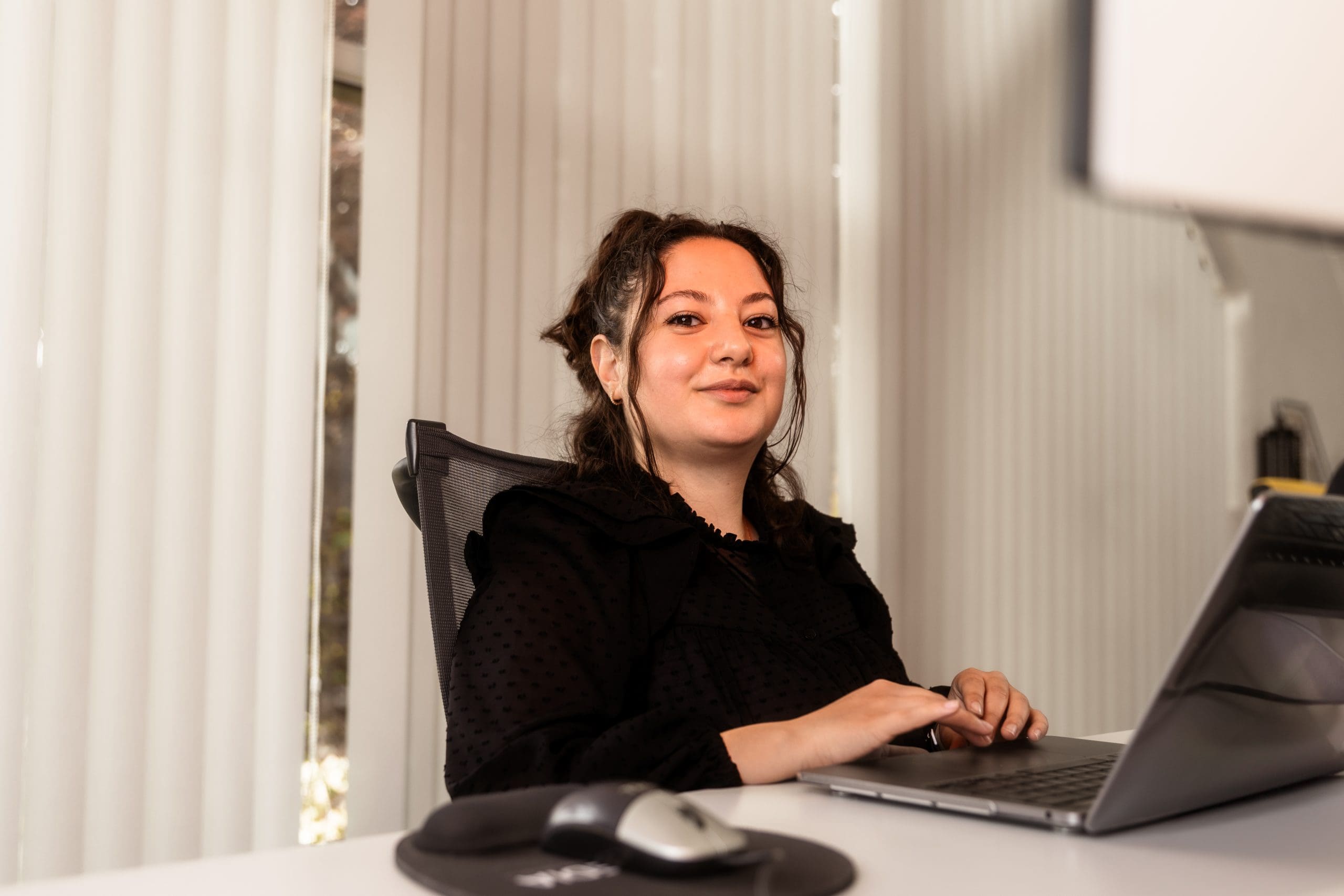 Merve Avci werkt glimlachend achter een laptop op kantoor