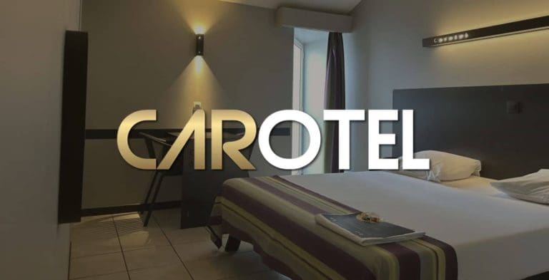 Carotel logo over hotelkamer met bed en wandverlichting