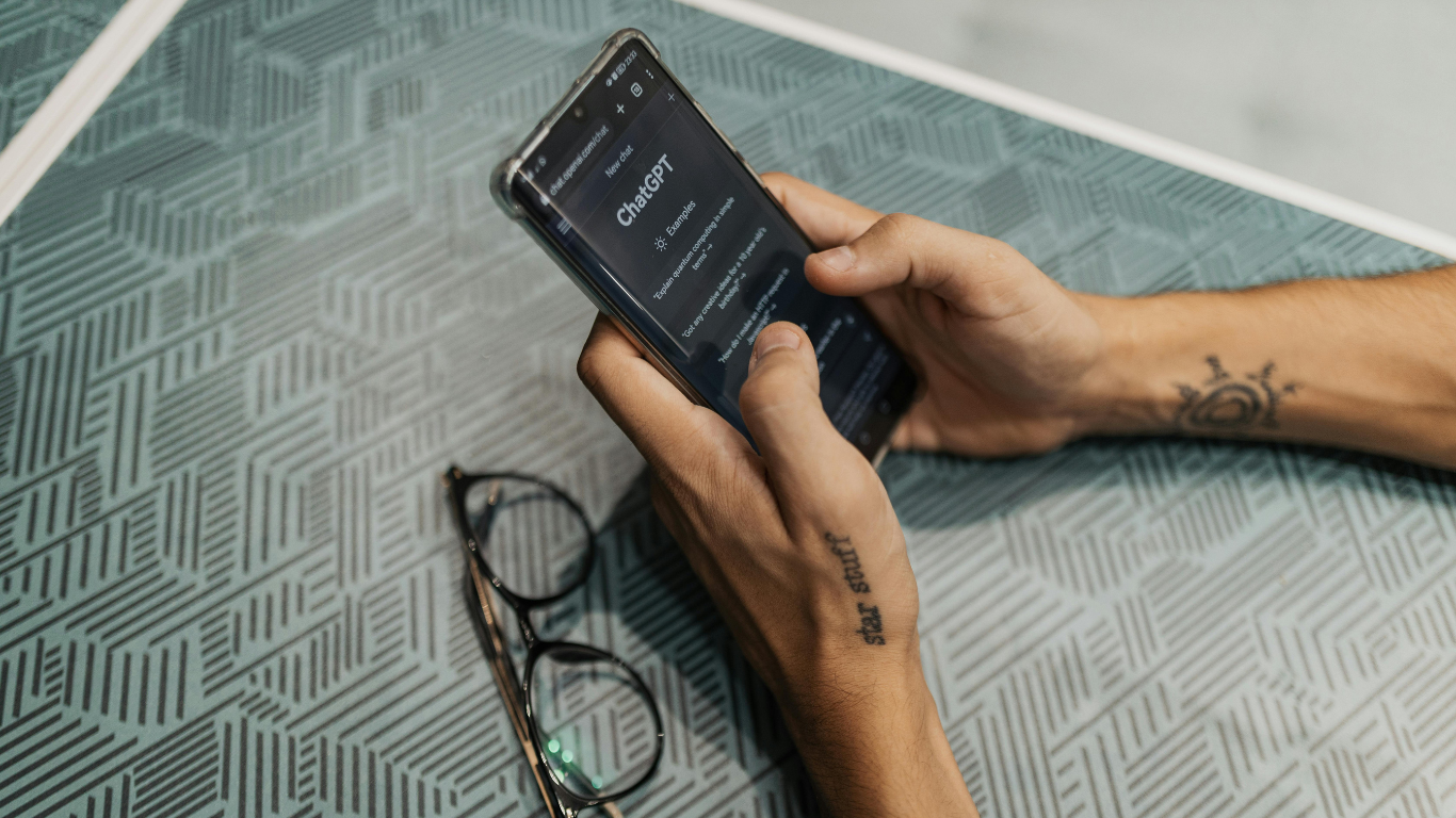 Persoon met tatoeage houdt smartphone vast naast een bril